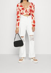 Top corto floreale color crema con fiori rossi, abbinato a jeans bianchi a zampa con dettagli strappati. Accessoriato con una borsa nera con texture.
