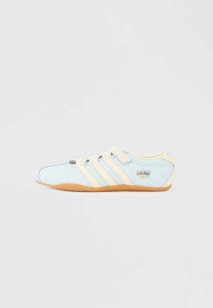 Lyseblå Adidas Tokyo-sneaker med beige tre striber, beige stropper og gummisål på en ensfarvet hvid baggrund.