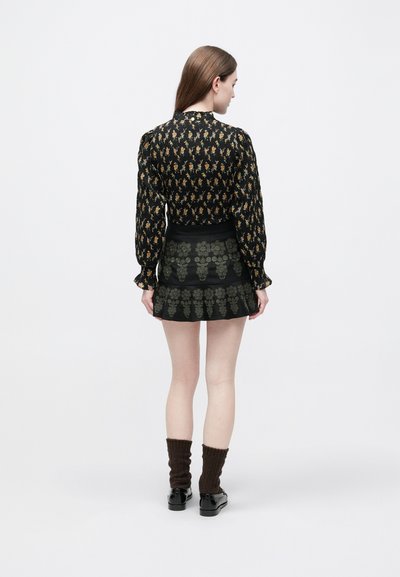 Μαύρη μακρυμάνικη μπλούζα με κίτρινα και πορτοκαλί λουλουδένια σχέδια· συνδυασμένη με μαύρη φούστα με πράσινο κεντητό σχέδιο και φουντωτό τελείωμα.