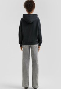 Czarna bluza z kapturem o luźnym kroju, ze ściągaczami przy rękawach i u dołu, zestawiona z szarymi dżinsami o prostych nogawkach i wysokim stanie. Matowe wykończenie.