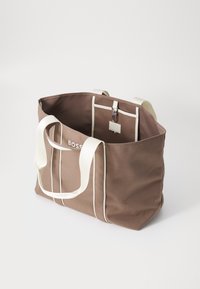 Bruine canvas draagtas met witte gestreepte accenten en handvatten, voorzien van een binnenzak en drukknopsluiting.
