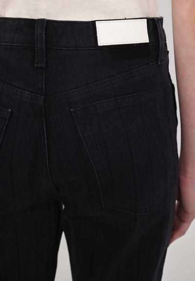 Jeans en denim noir avec un motif de rayures verticales, dotés d'une étiquette de marque en cuir blanc à l'arrière et d'un design minimaliste des poches arrière.