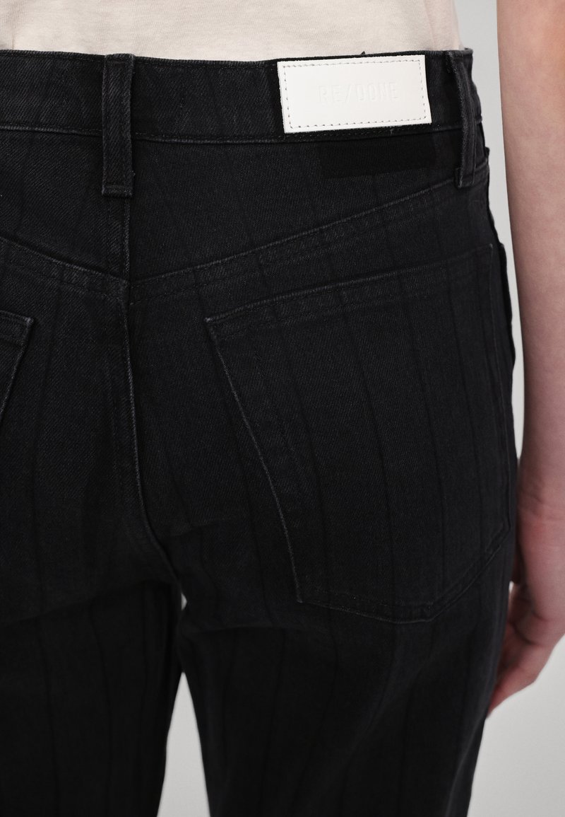 Jeans in denim nero con un motivo a righe verticali, dotati di un'etichetta in pelle bianca sul retro e di un design minimalista della tasca posteriore.