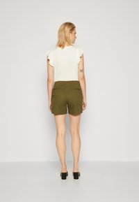 Top blanco de manga corta con mangas de volantes, combinado con pantalones cortos en color verde oliva. El conjunto presenta un diseño sencillo y una tela suave.