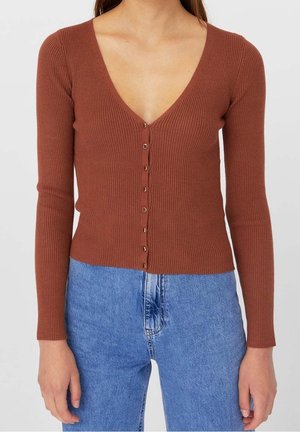 Femme portant un cardigan à boutons en maille côtelée brun avec des manches longues et un jean bleu taille haute, vu du cou aux hanches.