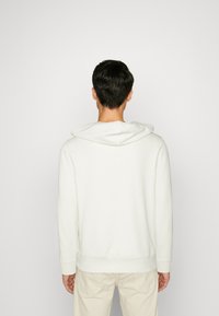 Sudadera blanca hecha de un tejido suave, con una capucha grande, puños y cintura acanalados, y un diseño simple y sin adornos.
