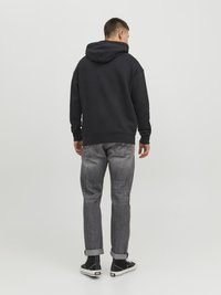 Black hooded sweatshirt, relaxed fit. Worn with faded, rolled-cuff gray jeans and black high-top sneakers. Simple, minimalist design.