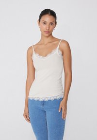Beige Top mit Spitzenbesatz, dünnen verstellbaren Trägern, einem gewellten Ausschnitt und Saum, aus weichem, dehnbarem Stoff gefertigt.