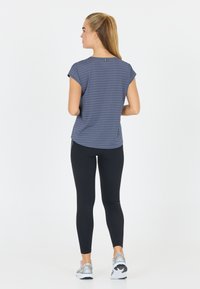Grårandig kortärmad topp i mjukt material, kombinerad med svarta leggings och sportskor, sedd bakifrån.