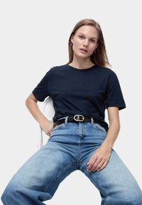 Mörkblå bomulls t-shirt, rund hals, kort ärm. Kombinerad med ljusblå högmidjade jeans och ett svart bälte med en guldspänne.