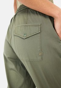 Olivengroene broek met een textuurafwerking, voorzien van een achterzak met een drukknoop en contrasterende stiksels.
