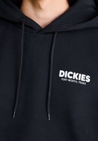 Sweat à capuche noir avec une poche kangourou, doté de cordons texturés et d'un logo blanc indiquant « DICKIES FORT WORTH, TEXAS ». Tissu doux.