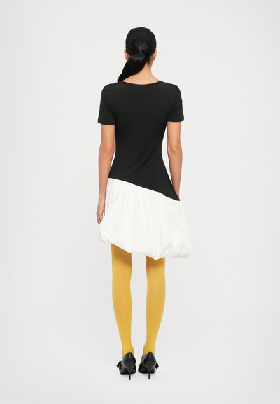 Zwarte fitted top met korte mouwen, witte ballonrok, gele panty's en zwarte hoge hakken. Gladde textuur, asymmetrisch ontwerp.