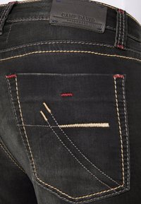 Schwarze Jeans aus Denim verfügen über eine Gesäßtasche mit kontrastierenden Nähten in Gelb, Rot und Weiß sowie einem Lederetikett am Bund.