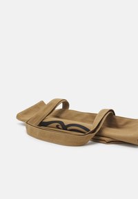 Beige kangaskassi, jossa on kaksi kangaskahvaa ja musta graafinen kuvio toisella sivulla. Kassi on pehmeä ja suorakulmion muotoinen.