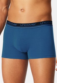 Blauwe boxershort met een diamantenpatroon, voorzien van een zwarte elastische tailleband met de tekst "uncover" in blauwe letters. Glad stoftextuur.