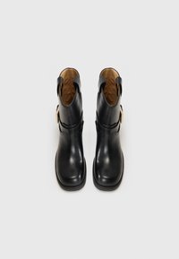 Botines de cuero negro con un acabado liso, punta redondeada, correas laterales y acentos de hardware en tono dorado. Interior forrado con material marrón.