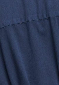 Tessuto blu navy con una texture liscia, caratterizzato da una cucitura orizzontale e una caduta morbida, che indica un design rilassato.