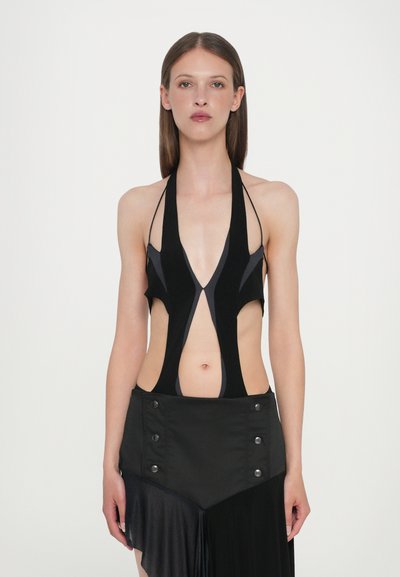 Haut en noir à encolure dégagée avec un design découpé, présentant une neckline plongeante et des accents gris contrastants. Associé à une jupe noire, mettant en avant des détails de boutons.