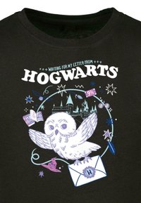 Sort t-shirt med grafik af en hvid ugle, brev, slot og stjerner, med teksten "Venter på mit brev fra Hogwarts."