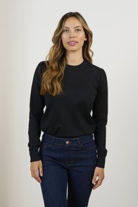 Maglione nero lavorato a maglia con colletto a giro e maniche lunghe, abbinato a jeans in denim blu scuro con chiusura a pulsante e cuciture a contrasto.