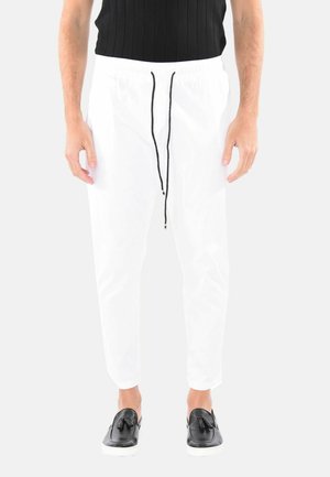 Pantaloni leggeri bianchi con vita elastica e cordino nero, caratterizzati da un design con gamba affusolata. Abbinati a scarpe nere senza lacci.