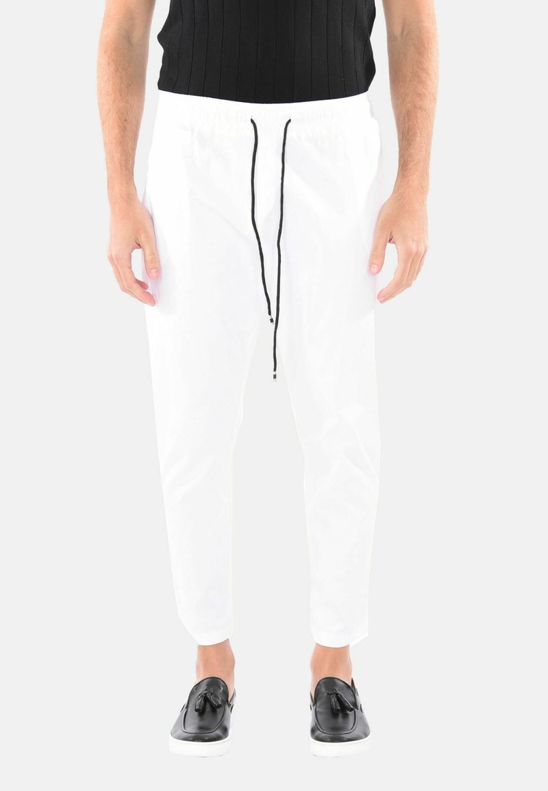 Pantaloni leggeri bianchi con vita elastica e cordino nero, caratterizzati da un design con gamba affusolata. Abbinati a scarpe nere senza lacci.