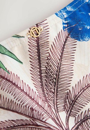 Tela floral con flores azules y hojas de helecho marrones sobre un fondo crema. Detalle de herrajes dorados en el borde. Textura suave.