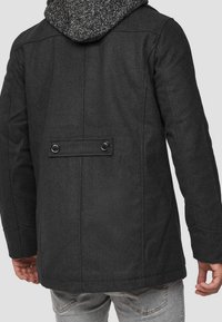 Giacca grigia scuro in misto lana con cappuccio, caratterizzata da tessuto strutturato, doppia fila di bottoni frontali e design posteriore semplice.