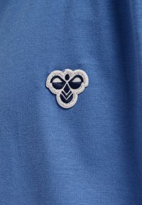 Blått tyg med en slät textur har en vit broderad bi-logo, detaljerade svarta accenter och intrikata designelement.