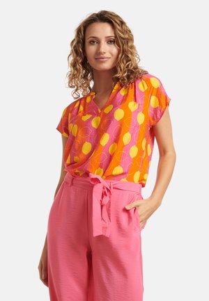 Vibrant orange and pink blouse with yellow balloon patterns; loose fit, short sleeves, and a V-neck design. Paired with pink high-waisted pants.