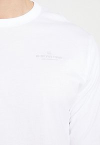 Vit långärmad t-shirt i bomull med rund halsringning. Har en subtil, präglad logo på bröstet med texten "G-Star RAW."