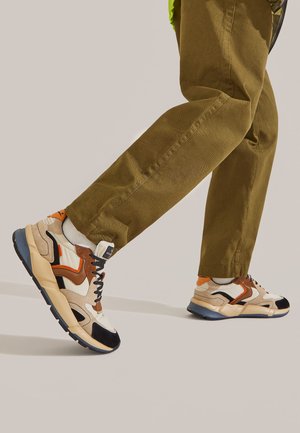 Multifarvede atletiske sneakers med en blanding af beige, brun, marineblå og orange accenter, med et chunky såledesign og teksturerede materialer.