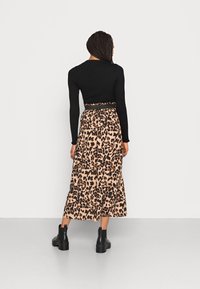 Schwarzes geripptes Langarmshirt kombiniert mit einem beigen Maxirock im Leopardenmuster. Das Model trägt schwarze Stiefeletten. Einfaches, fließendes Design.