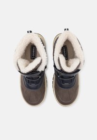 Par de botas de invierno de color marrón oscuro y azul marino con forro de lana beige y suelas beige, vistas desde arriba sobre un fondo blanco.