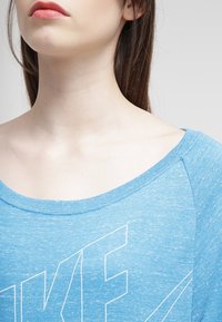 Blå, heathered bomulls t-shirt med vid halsringning, korta ärmar och en vit "NIKE" logo tryckt på framsidan. Slät struktur.