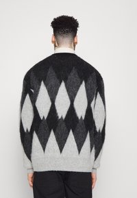 Stickad tröja i grått och svart med ett diamantmönster, som har en något lös passform, rund hals och långa ärmar. Sträv struktur.