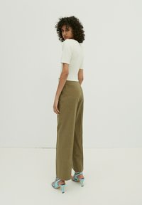 Geknipte witte ribbed top, olijfgroene wijde broek en blauwe strappy hakken. Model staat met de rug naar de camera gekeerd, waardoor de details van de outfit zichtbaar zijn.