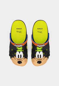 Ζευγάρι μαύρων και νέον κίτρινων Crocs χωρίς κορδόνια με το πρόσωπο του Γκούφυ στο μπροστινό μέρος και πορτοκαλί λουριά με την ετικέτα «Goofy» σε λευκό φόντο.