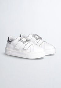 Hvide sneakers med velcro-stropper, prydet med en dekorativ sølvkæde, glat læder, en struktureret gummisål og et diskret logo på siden.