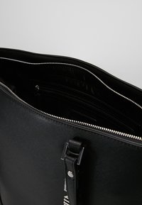 Černá kožená taška s texturovaným povrchem, stříbrným zipem a vnitřními přihrádkami. Design má elegantní, obdélníkový tvar.