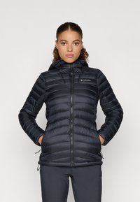 Czarna kurtka puchowa z kapturem, pikowana, z zamkiem błyskawicznym z przodu oraz logo Columbia na piersi. Posiada sznurki regulacyjne przy dolnej krawędzi.