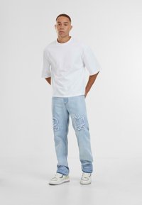 T-shirt blanc à manches courtes associé à un jean bleu clair déchiré avec de grands accents brodés et des baskets blanches.