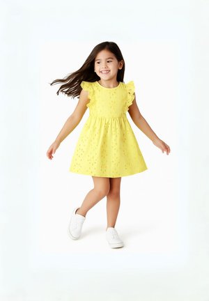 Abito giallo con maniche arricciate, tessuto textured con motivi floreali ritagliati e gonna a ruota, abbinato a sneakers bianche.