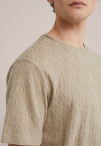 Beige kötött póló, geometrikus textúrával és rövid ujjakkal, kerek nyakkivágással és sima, puha felülettel.