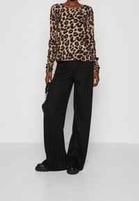 Haut à manches longues en imprimé léopard en tissu doux, associé à un pantalon large noir et des baskets noires épaisses. Texture lisse et coupe décontractée.