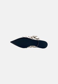 Scarpa con punta affusolata e upper bianco, con più cinturini e una suola nera bassa. Dettaglio in metallo vicino alla caviglia.