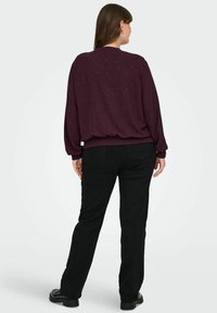 Bordo dukserica s točkastim uzorkom, rebrastim manžetama i donjim rubom. Crne hlače ravnog kroja s džepovima i crne cipele, minimalnog detaljiranja.