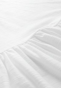Tissu blanc texturé avec des détails élastiques froncés, montrant des plis doux et de subtiles lignes horizontales à la lumière naturelle.