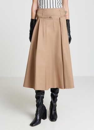 Jupe trapèze beige avec un design plissé, dotée d'une ceinture subtile et d'un détail métallique. Associée à des gants noirs ajustés et des bottes noires montant jusqu'aux genoux.